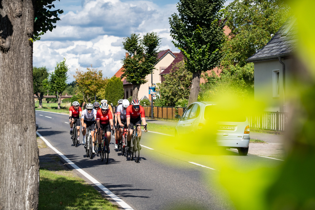 Cyclists in a group on a country road with houses and trees in the background
